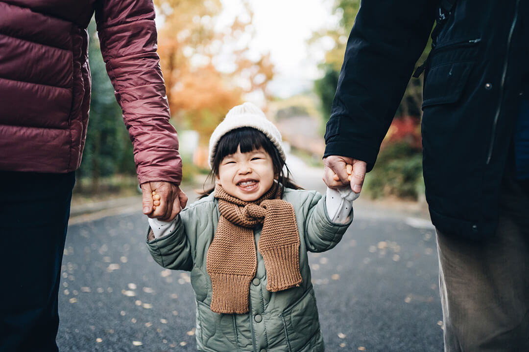Young girl out on a walk smiling whilst holding hands with parents